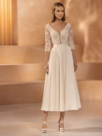 A woman in a cream-colored midi dress with lace sleeves.